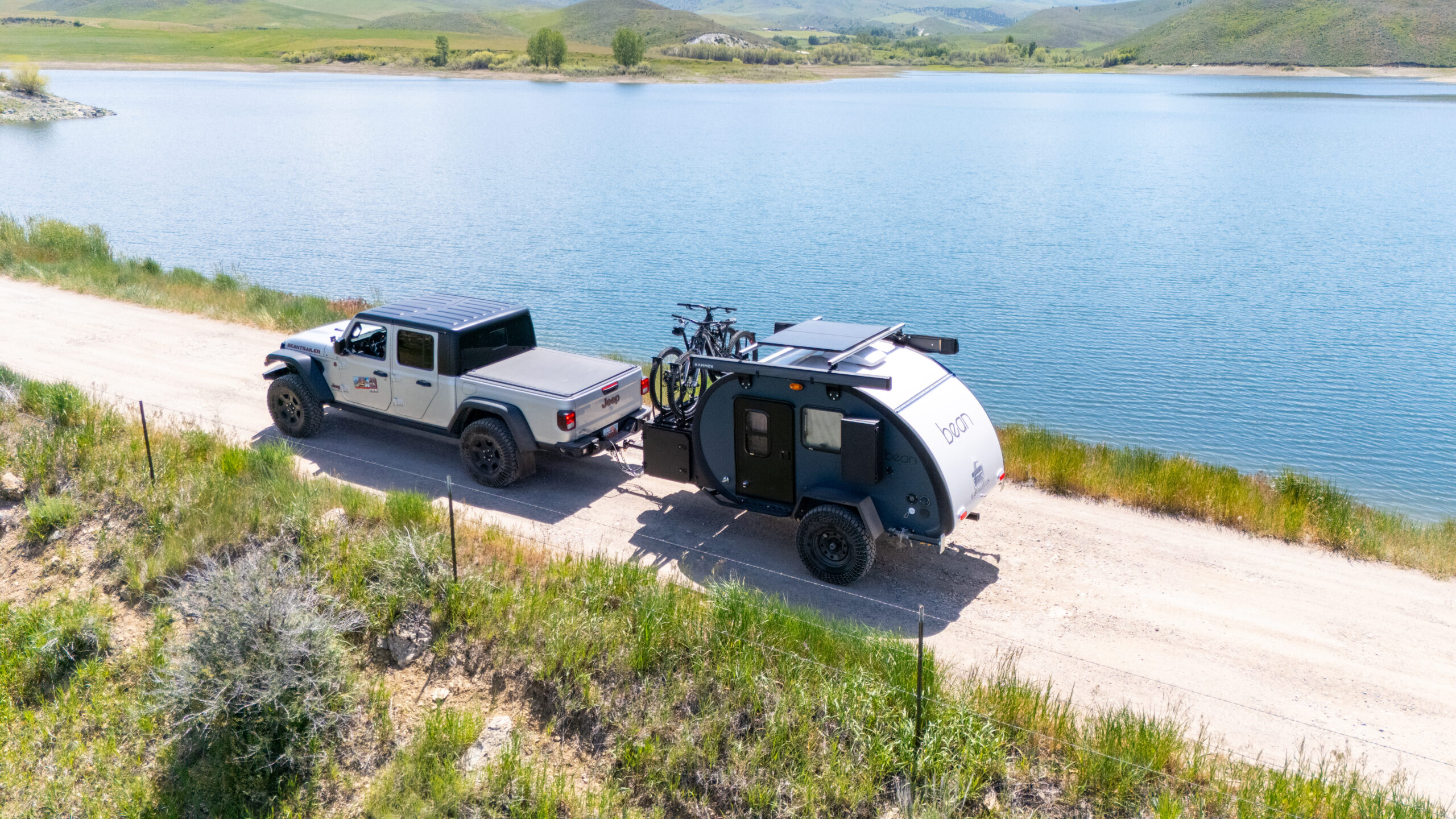 A Meaner Bean towed along a lakeside dirt road behind a pickup