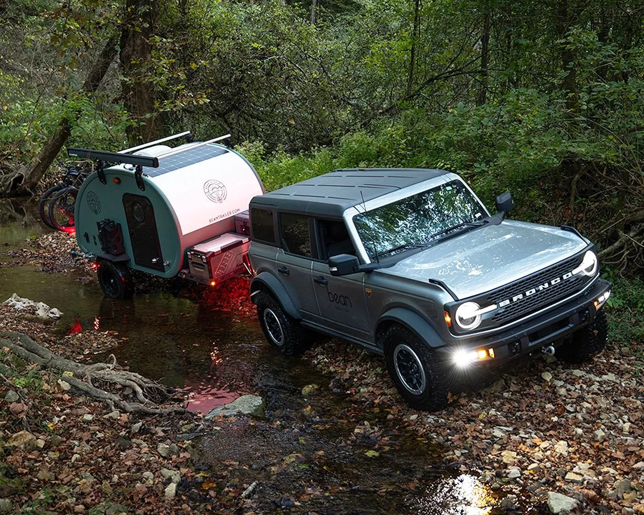 Bean Stock 2.0 behind a pickup at a sandy creek crossing under a sunset sky