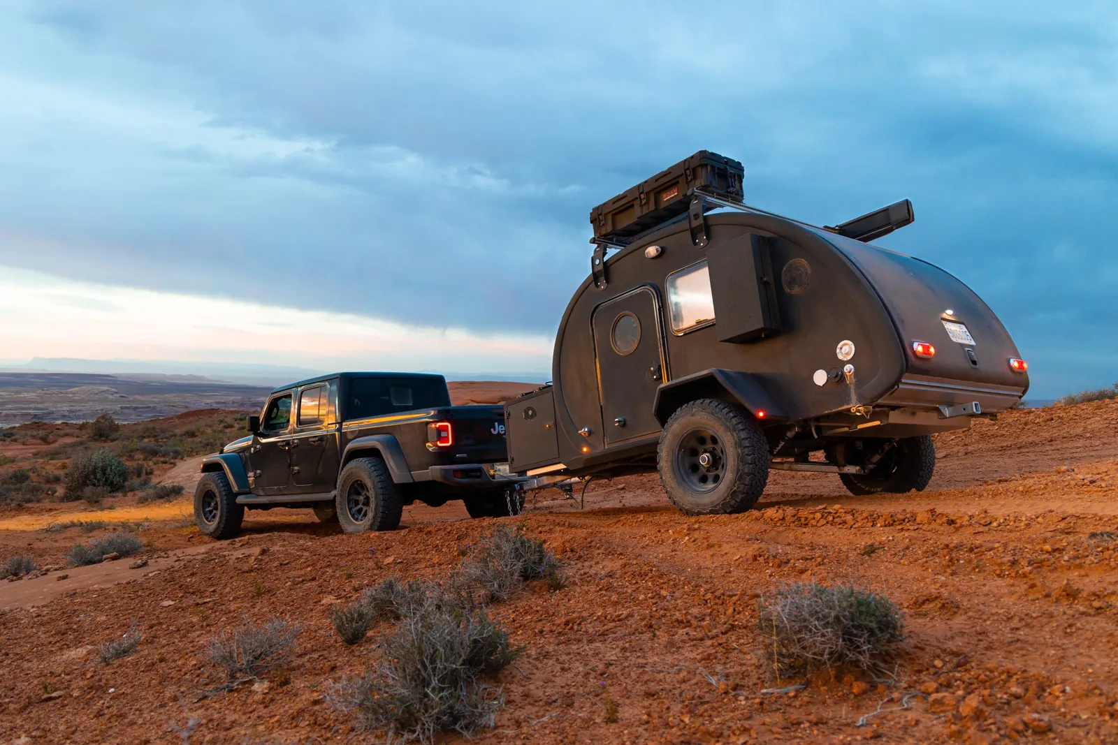 Black Bean behind a Jeep Gladiator on red desert dirt at dusk