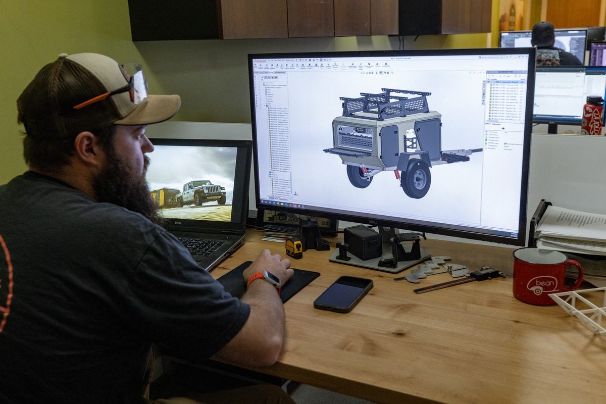 An engineer at a desk with a 3D CAD model of a Bean trailer on the monitor