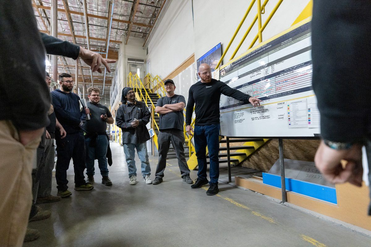 Bean team members gathered around a whiteboard on the plant floor