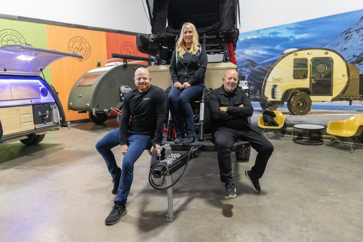 Brian, Cindy and Mark sitting on a Bean in front of other Bean trailers and a colorful wall